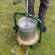 Fruktpress Original 12L En vuxen man använder en cylinderformad fruktpress i rostfritt stål och gröna detaljer utomhus i trädgården